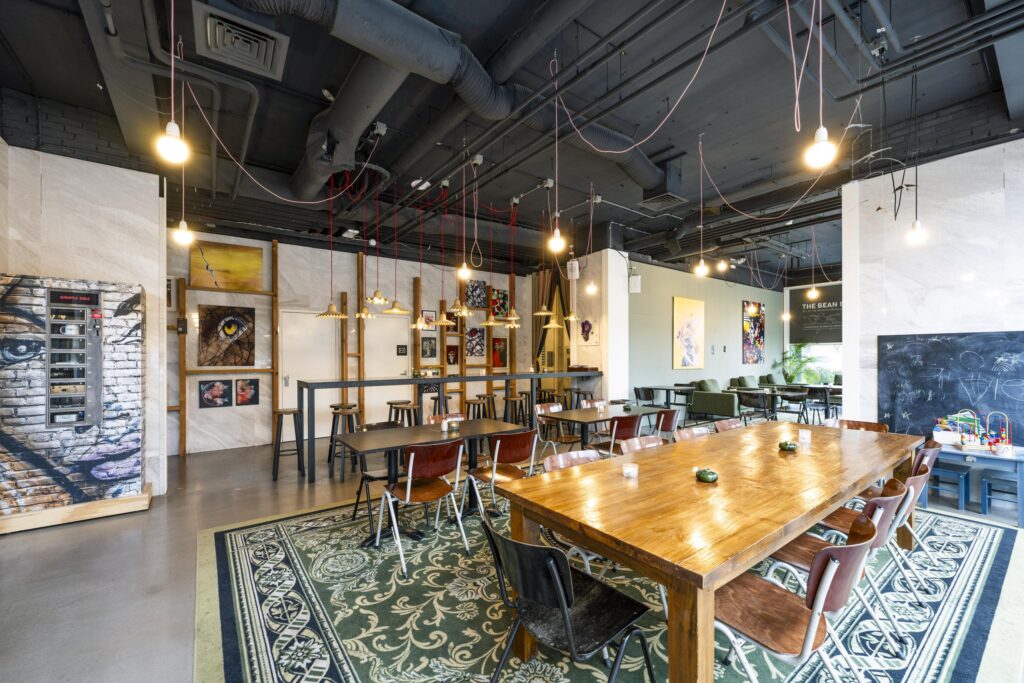 Modern shared workspace with wooden tables, eclectic artwork, and industrial ceiling at Laan van Kronenburg.